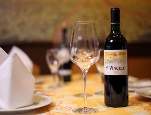 Flasche Rotwein und leeres Glas auf fein gedecktem Tisch mit gefalteten weißen Servietten in elegantem Restaurant