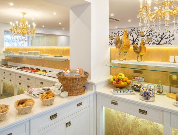 Helles Frühstücksbuffet im Hotel mit frischem Brot, gekochten Eiern, Obstschale, kalten Aufschnitt, goldenen Kronleuchtern und Dekohähnen