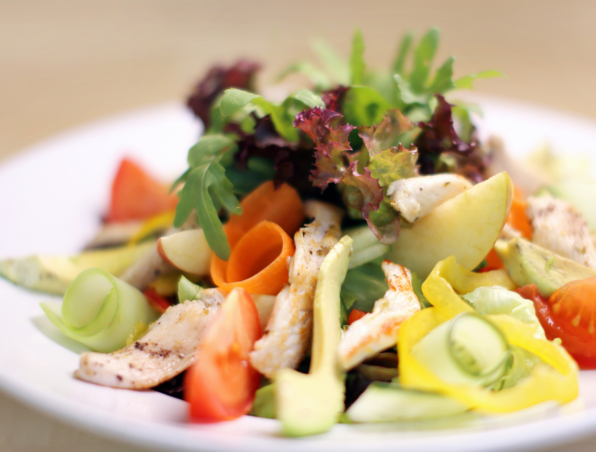 Frischer gemischter Salat mit gegrilltem Hähnchen, Tomaten, Gurkenstreifen, gelber Paprika, Avocado und Blattsalat auf weißem Teller