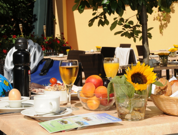 Frühstück im Freien mit Obstschale, Saft, Kaffee, Brotkorb und Sonnenblumen-Dekoration auf Hotelterrasse