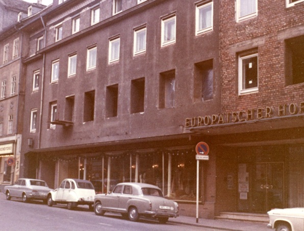 Historisches Hotelgebäude mit altmodischen Autos davor, großen Schaufenstern und klassischer europäischer Fassade