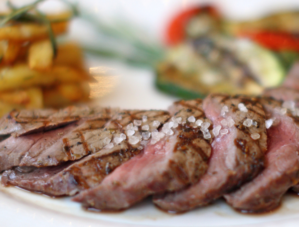 Gegrillte Steakstreifen medium rare mit grobem Meersalz, dazu gewürzte Pommes und gemischtes Grillgemüse.