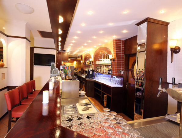 Gemütliche Hotelbar mit poliertem dunklem Holztresen, roten Lederstühlen, warmem Licht und gut bestückten Spirituosenregalen unter Ziegelbögen.