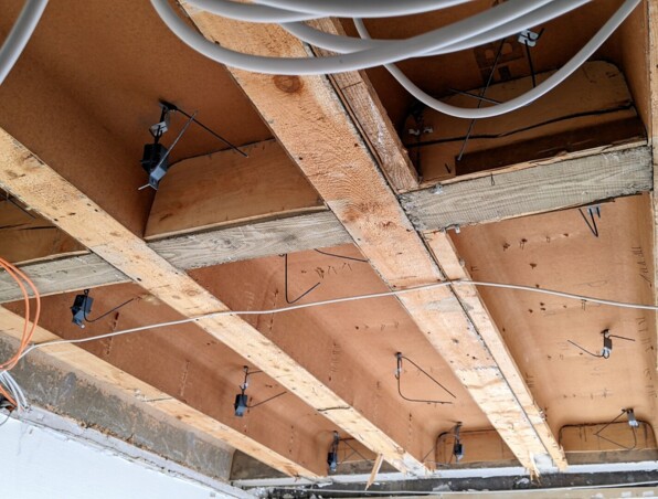 Exposed ceiling beams with electrical wiring and mounting brackets in a building under renovation.