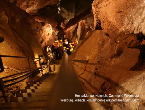 Geführte Gruppe mit Schutzhelmen erkundet beleuchtete unterirdische Höhle, geht Treppen zwischen felsigen Wänden hinab