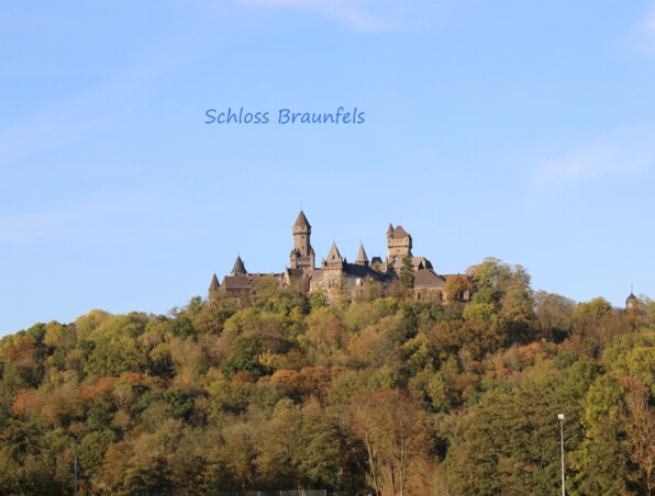 Historisches Schloss Braunfels auf bewaldetem Hügel mit herbstlichem Laub unter klarem blauem Himmel