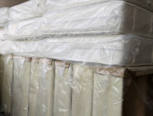 Stacked new mattresses wrapped in protective plastic, ready for hotel room setup or replacement.