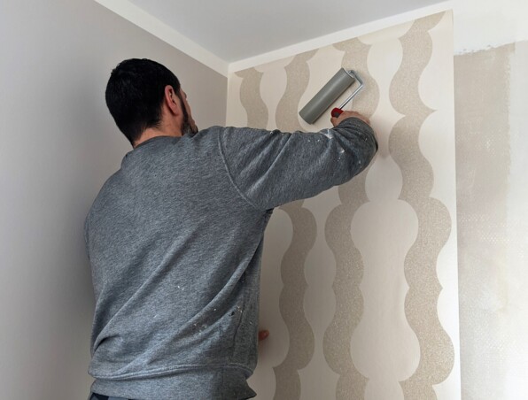 Hotel staff applying modern beige wallpaper with a textured wave pattern in a guest room for a fresh updated look