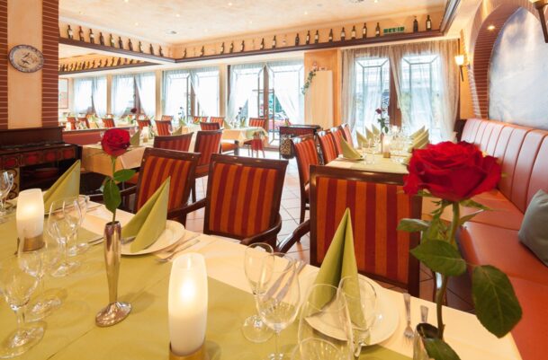 Cozy hotel restaurant with striped chairs, soft lighting, red roses on tables, and sheer curtains letting in natural light