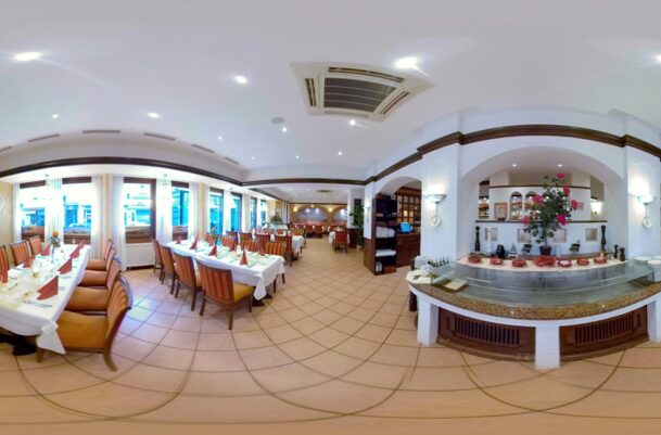 Spacious hotel dining room with neatly set tables, warm lighting, tiled floors, and floral centerpieces for elegant meals