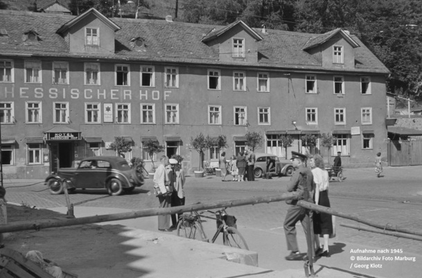 Historisches Hotel Hessischer Hof mit klassischen Autos und Gästen in zeittypischer Kleidung auf ruhigem Stadtplatz