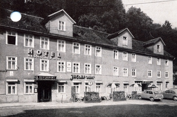 Historisches dreistöckiges Hotel mit zahlreichen Fenstern, Außenbereich mit Sonnenschirmen und Oldtimerautos vor dem Eingang