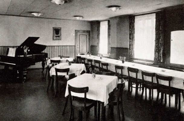 Vintage Speiseraum im Hotel mit weißen Tischdecken, Holzstühlen, großen Fenstern mit Vorhängen und einem Flügel in der Ecke