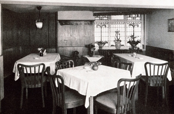 Gemütlicher Speiseraum mit Holzmöbeln, weißen Tischdecken, Buntglasfenstern und Blumenarrangements für klassische Atmosphäre