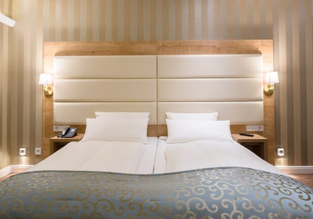 Modern twin beds with white padded headboard, bedside tables, soft wall lamps, and a blue patterned bed runner