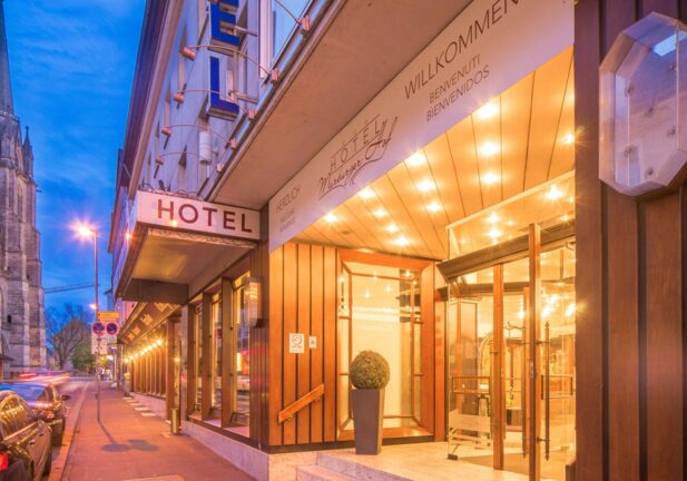 Warmly lit hotel entrance with glass doors and modern wooden paneling on a quiet city street at dusk
