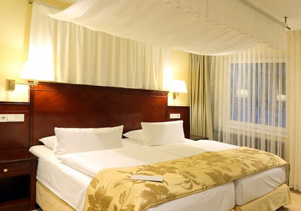 Elegantes Hotelzimmer mit zusammengestellten Einzelbetten, Holz-Kopfteil, warmem Gelblicht und transparenten Vorhängen