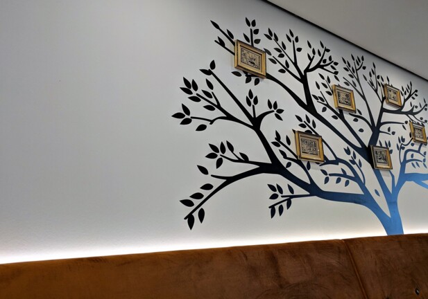 Moderner Hotel-Loungebereich mit brauner Polsterbank vor einer Wand mit schwarzem Baum-Wandbild und kleinen gerahmten Kunstwerken