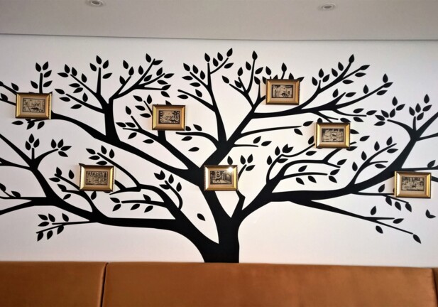 Dekoratives schwarzes Baum-Wandbild mit sechs kleinen gerahmten Vintage-Bildern über hellbraunem Polstersofa in Hotel-Lounge