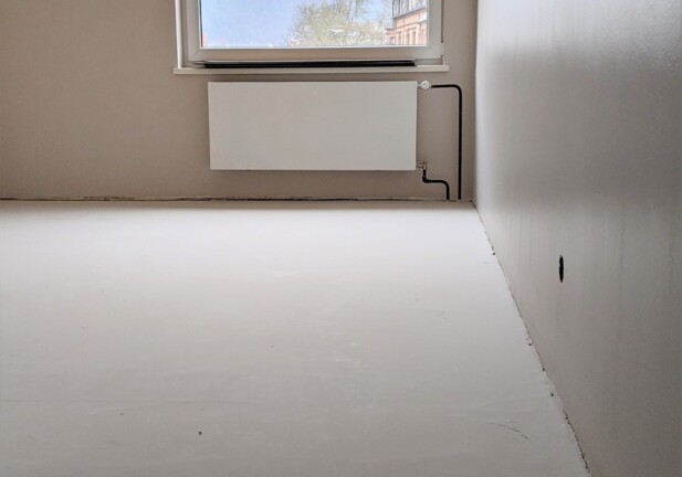 Empty unfinished hotel room with smooth light walls, a radiator under a window showcasing a mountain and historic building view
