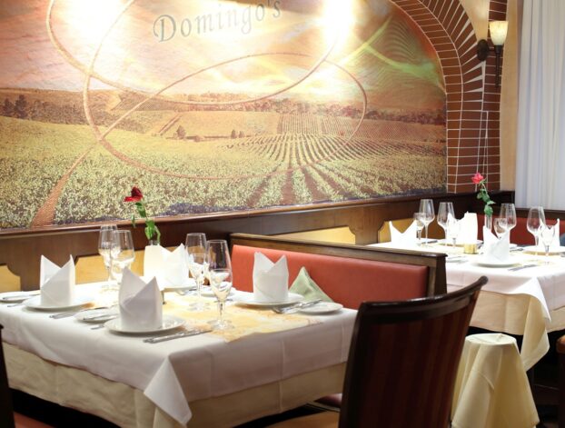 Eleganter Restaurantbereich mit weißen Tischdecken, gefalteten Servietten, Weingläsern und Wandmalerei eines Weinbergs