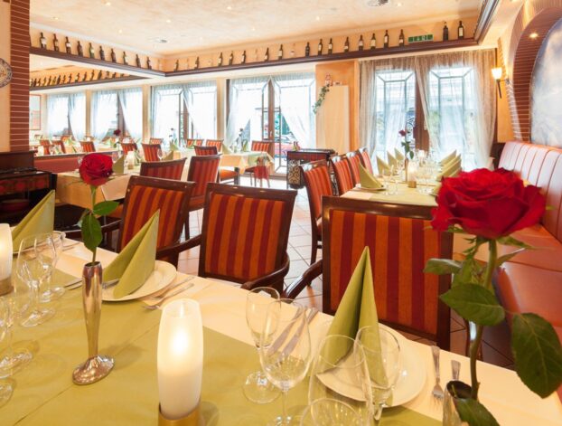 Helles Restaurant mit gestreiften Stühlen, grünen Servietten, roten Rosen in Vasen und sanfter Beleuchtung