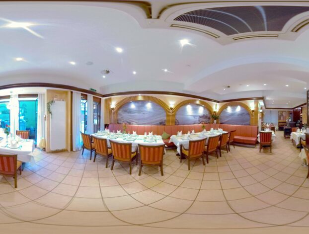 Elegantes Hotelrestaurant mit sorgfältig gedeckten Tischen, gepolsterten Sitzbänken, gewölbter Wanddekoration und heller Beleuchtung.