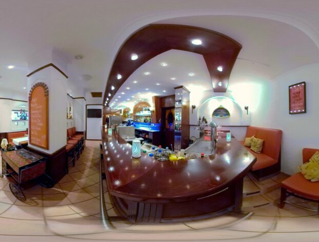 Gemütliche Hotelbar mit gebogenem Holztheken, gepolsterten orangen Sitzen, sanfter Beleuchtung und floralen Wandbildern