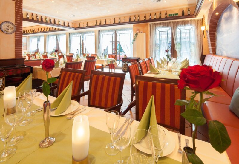 Helles Restaurant mit gestreiften Stühlen, grünen Servietten, roten Rosen in Vasen und sanfter Beleuchtung