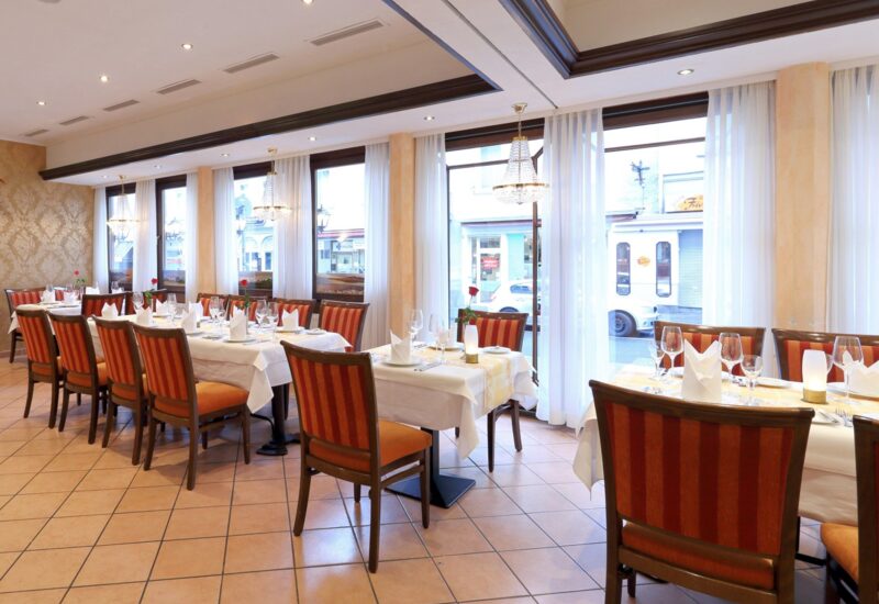 Eleganter Hotelrestaurant mit gestreiften Polsterstühlen, weißen Tischdecken, Kristallleuchtern und großen Fenstern mit transparenten Vorhängen