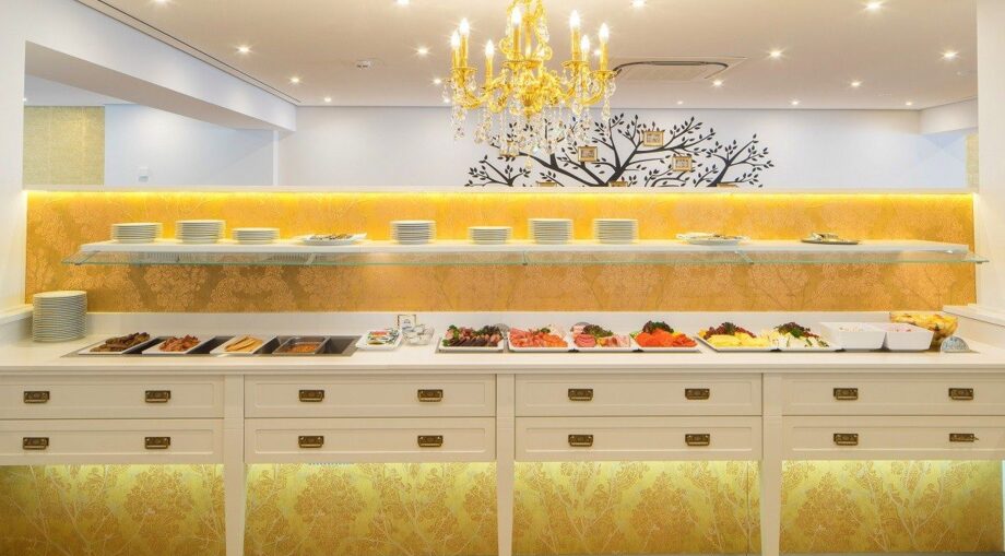 Elegant breakfast buffet with cold cuts, cheeses, and pastries under a golden chandelier and modern decor