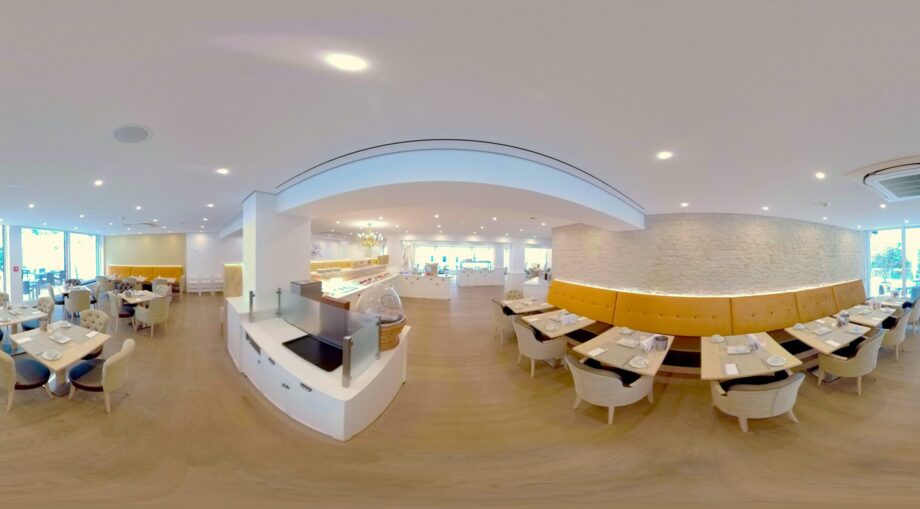 Bright hotel restaurant with tufted chairs, yellow banquette seating, wood floors, buffet area, and large windows opening to outdoor dining