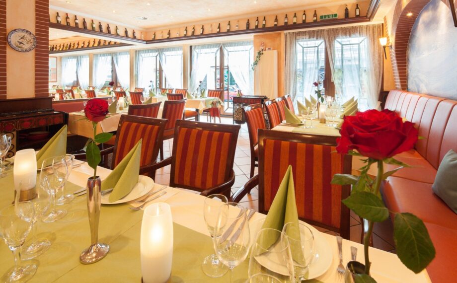 Helles Restaurant mit gestreiften Stühlen, grünen Servietten, roten Rosen in Vasen und sanfter Beleuchtung