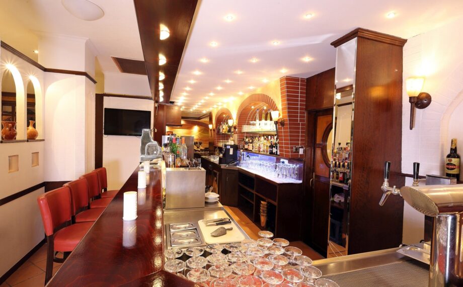 Gemütliche Hotelbar mit poliertem Holztresen, roten Polsterstühlen, Backsteinbögen mit Spirituosen und stimmungsvoller Beleuchtung