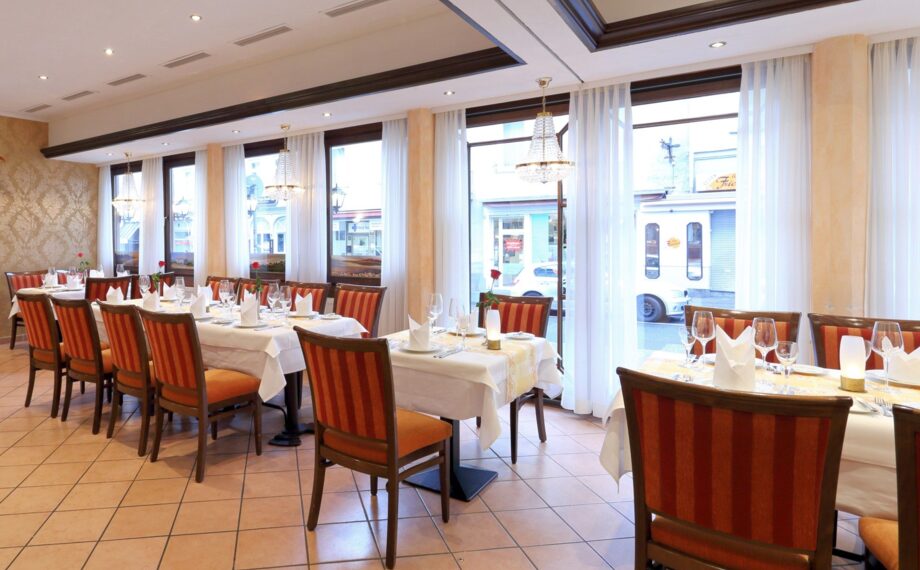 Eleganter Hotelrestaurant mit gestreiften Polsterstühlen, weißen Tischdecken, Kristallleuchtern und großen Fenstern mit transparenten Vorhängen