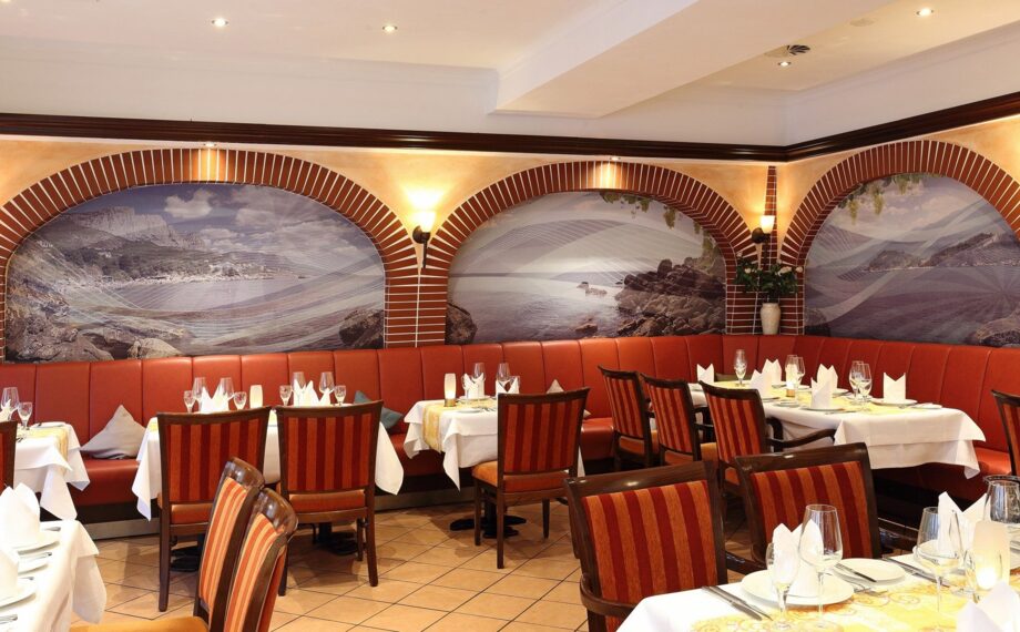 Eleganter hotelrestaurantbereich mit rotem Leder-Sitzbank, gestreiften Holzstühlen, weißen Tischdecken und Küstenmuralen an gewölbten Wänden