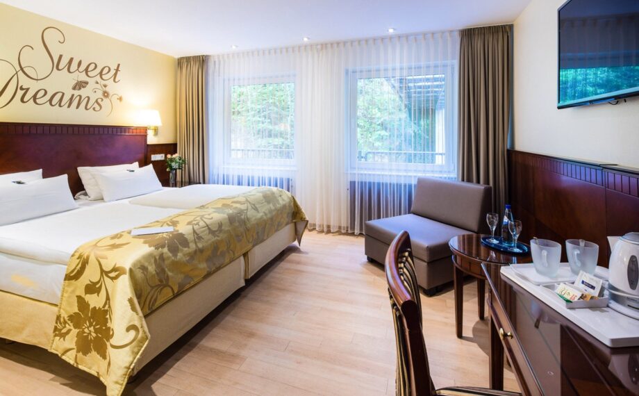 Helles Hotelzimmer mit Doppelbett, elegantem goldenen Überwurf, Wanddekoration mit 'Sweet Dreams', Sitzgelegenheit und Teebereiter