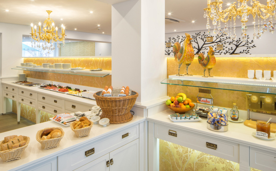 Helles Frühstücksbuffet im Hotel mit frischem Brot, gekochten Eiern, Obstschale, kalten Aufschnitt, goldenen Kronleuchtern und Dekohähnen