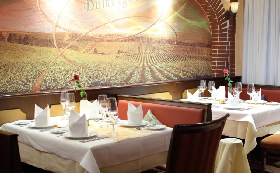 Elegante Restaurantbestuhlung mit weißen Tischdecken, Servietten, Weingläsern, roter Ledersitzbank und Weinberg-Wandbild