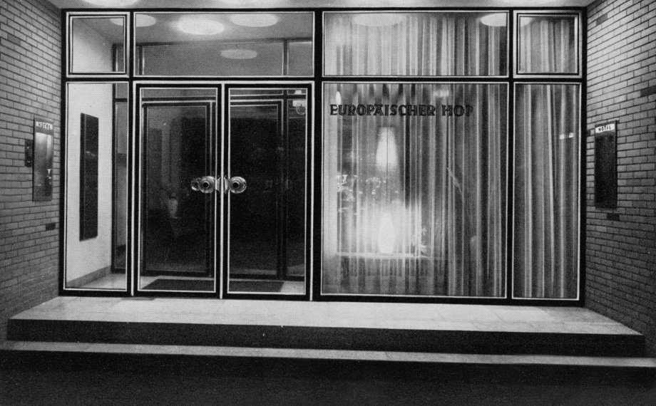 Moderner Hoteleingang mit doppelflügeligen Glastüren, großen Fenstern und Backsteinwänden, beleuchtet von Deckenleuchten