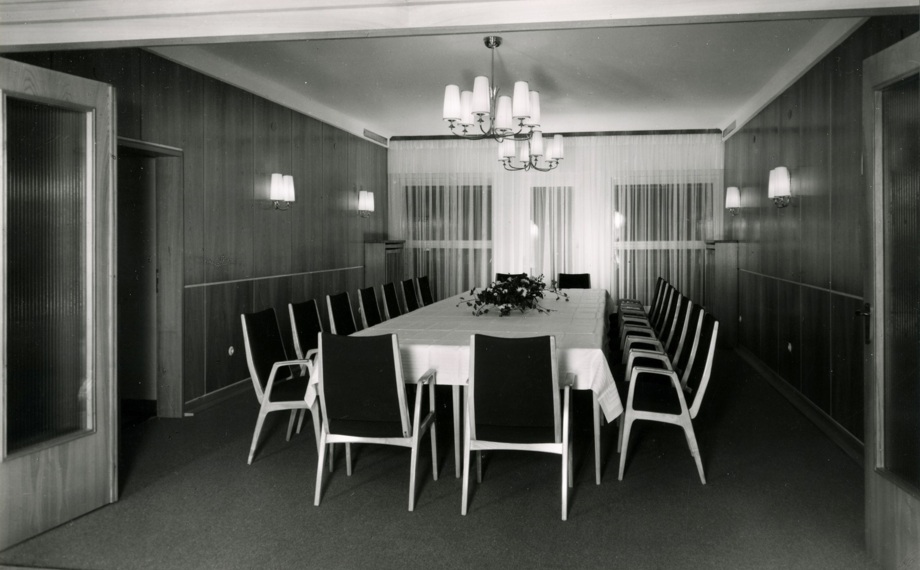 Klassischer Konferenzraum mit langem Tisch, vierzehn Stühlen, holzvertäfelten Wänden, Wandlampen und zentralen Kronleuchtern