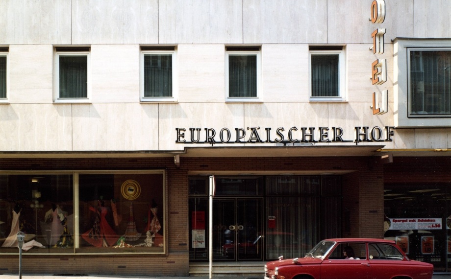 Moderne Hotel-Fassade mit großen Fenstern, dem Vintage-Schild 'Europäischer Hof' und einem klassischen roten Auto davor