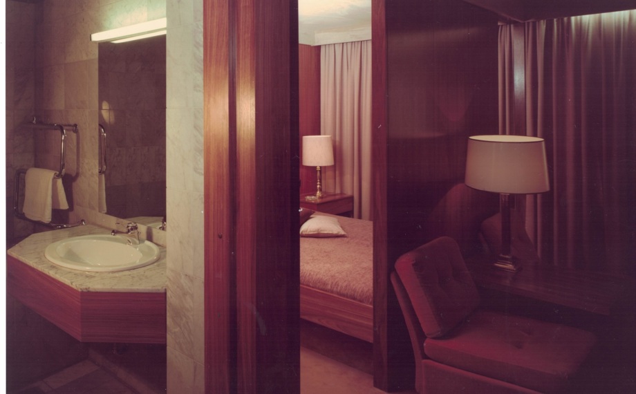 Gemütliches Hotelzimmer mit Holzakzenten, Nachttischlampe, Einzelbett und Marmorwaschbecken mit Handtuchhalter