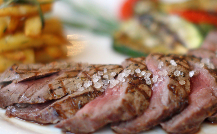 Gegrillte Steakstreifen medium rare mit grobem Meersalz, dazu gewürzte Pommes und gemischtes Grillgemüse.