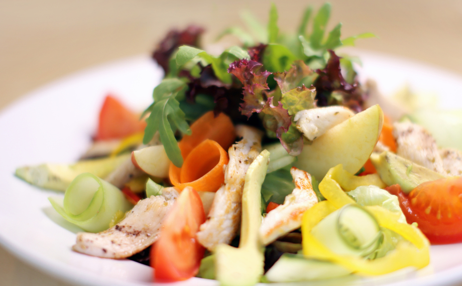 Frischer Gartensalat mit gegrilltem Hähnchen, gemischtem Grün, Tomatenspalten, Gurkenbändern und Karottenröllchen auf weißem Teller