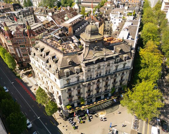 Großes historisches Hotel mit prächtiger Fassade, Dachterrasse, Straßencafé und baumgesäumter Allee.