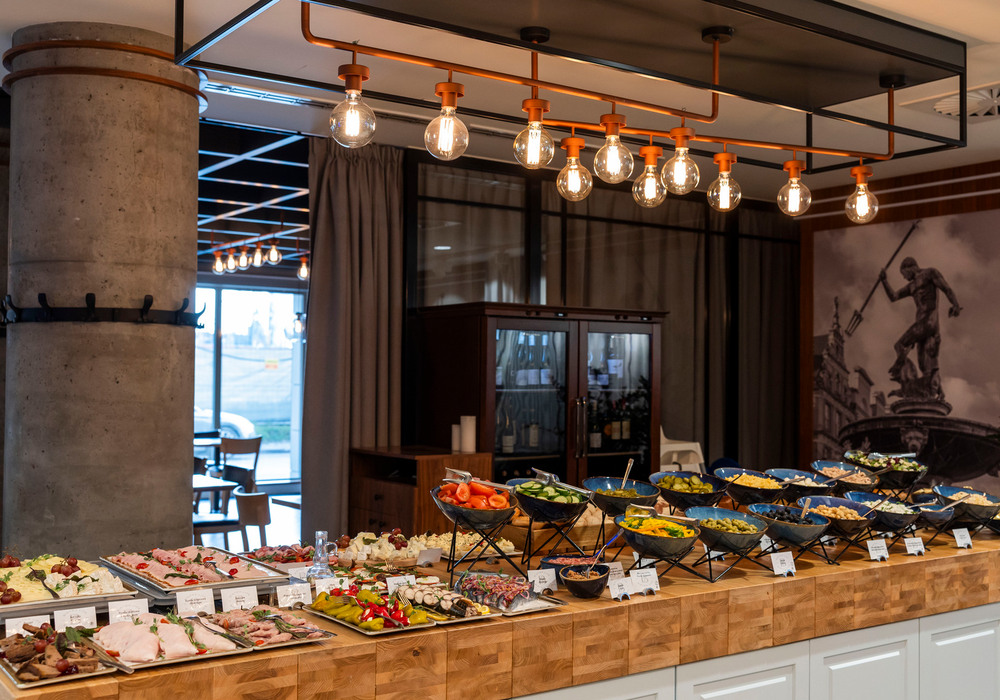 Generous hotel buffet of cold cuts, cheeses and salad bowls on a wooden counter beneath warm pendant lights