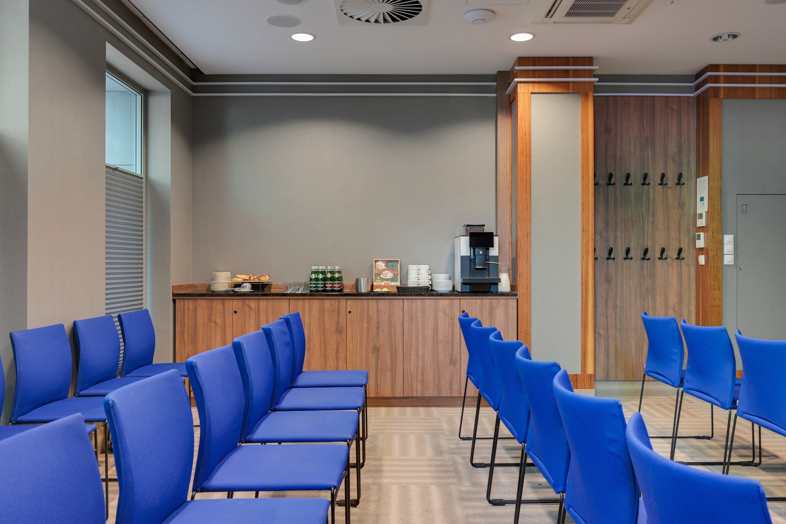 Konferensrum med rader av blå stolar, kaffestation, bakverk och garderobskrokar