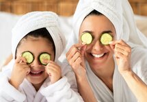 Matka i dziecko w białych szlafrokach i turbanach z ręczników trzymają plasterki ogórka na oczach, relaks w hotelowym spa