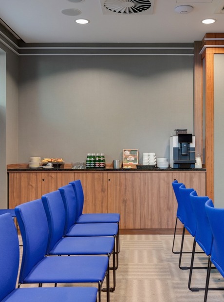 Conference room with rows of blue chairs, self-serve coffee station, pastries and wall coat hooks